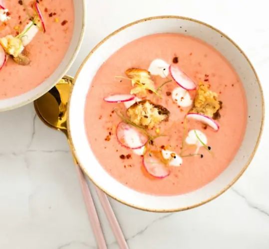 An presentation of a homemade and traditional pink soup made during the Pink Soup Festival topped with fresh ingredients and warm broth.